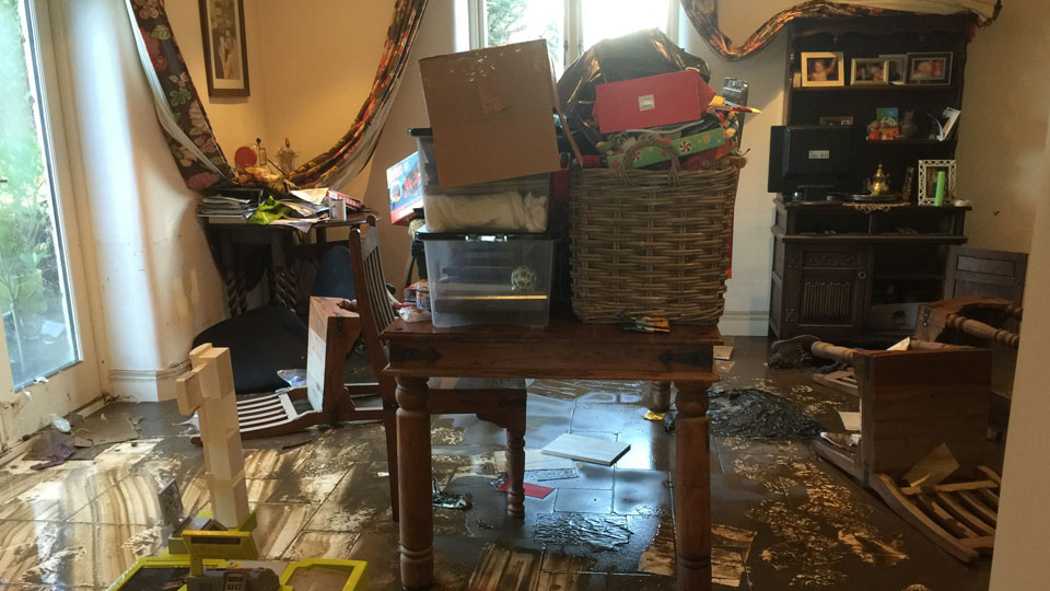 Flood damage to a home in Whalley (2015), the floor is muddy and possessions are stacked on tables, etc